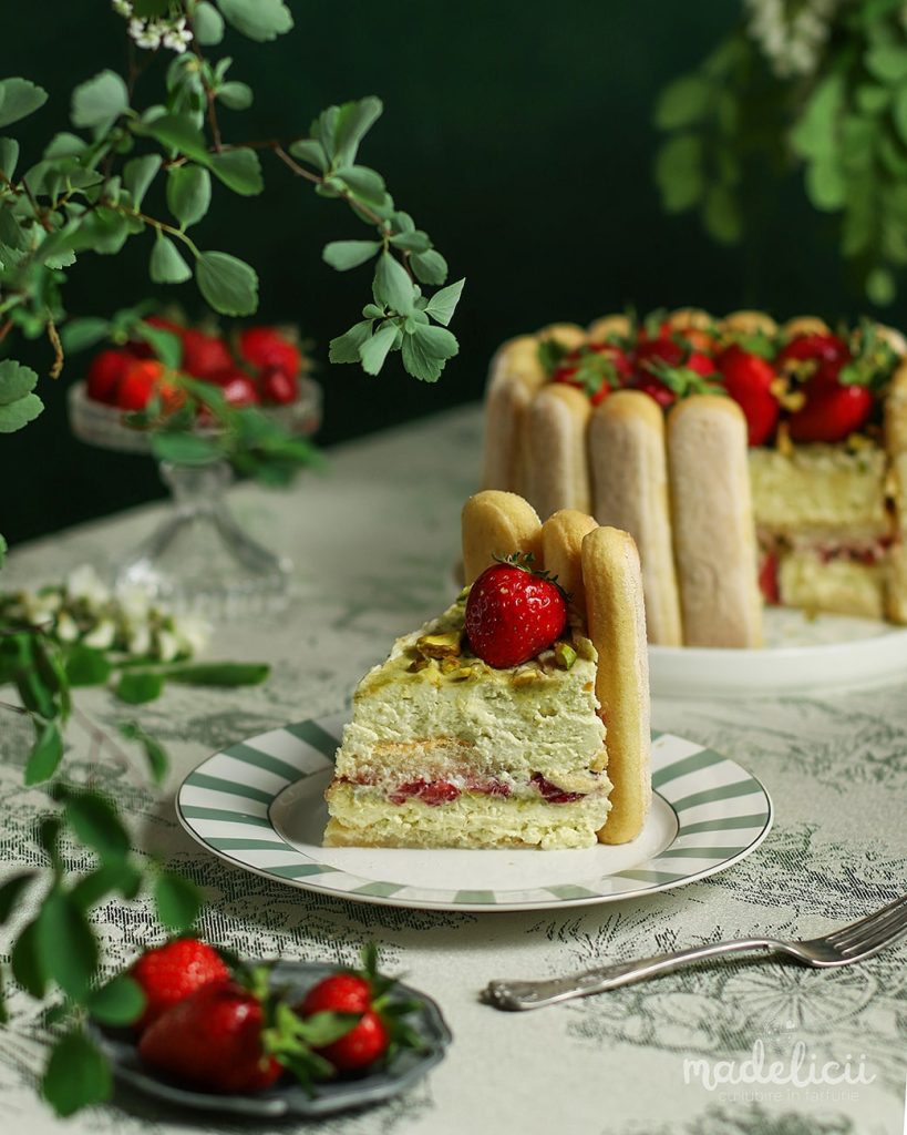 Felie de tort tiramisu cu fistic si capsuni, cu straturi de crema de mascarpone si fistic, piscoturi insiropate si capsuni proaspete.